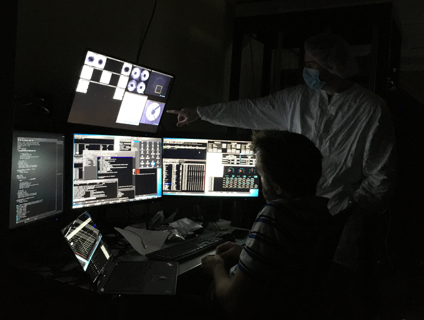 Alex Hedglen, in full cleanroom getup, points to an image of the MagAO-X pupil on one of Jared's five screens full of MagAO-X control software.