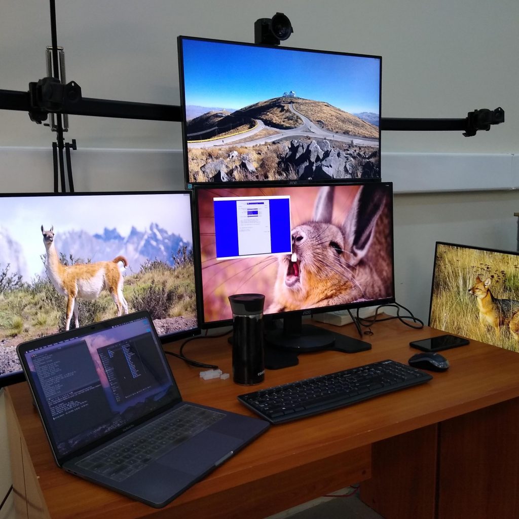 Four computer monitors are visible, three sitting on a desk and one on a mount. The mount has positions for all four, but only one is occupied.