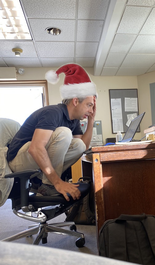 Olivier Guyon working on his laptop while perched awkwardly on a chair (with a photoshopped Santa Claus hat).