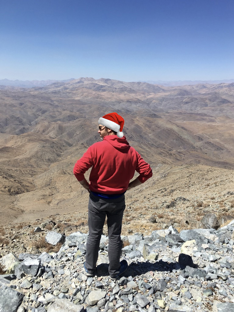 Jared surveys the rocky mountainside, looking into the distant Atacama with a photoshopped Santa Claus hat.